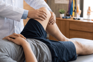 Medical professional bending and examining a patient’s knee while the patient lies on an exam table in a clinical setting.
